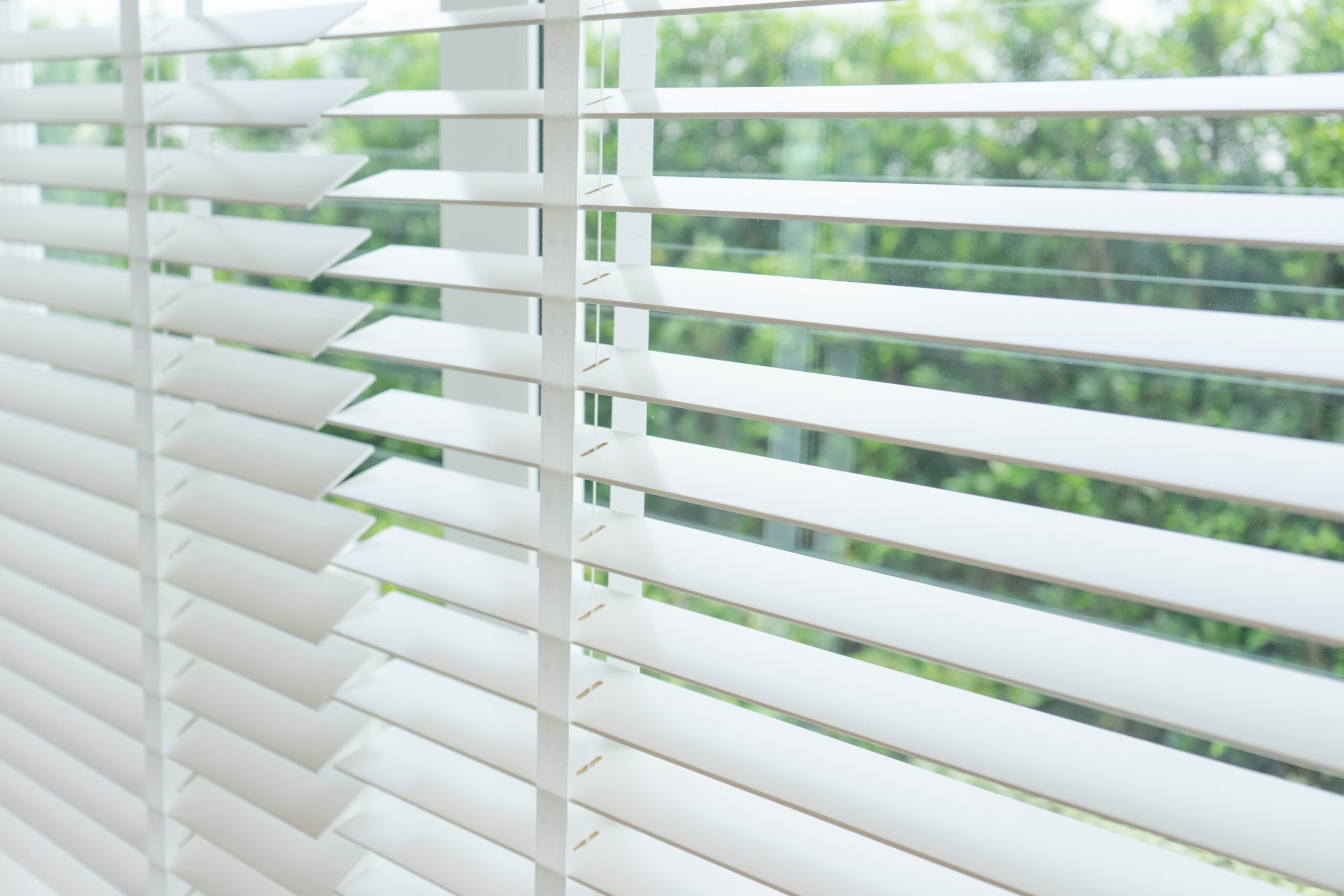 white faux wood blinds open on a window