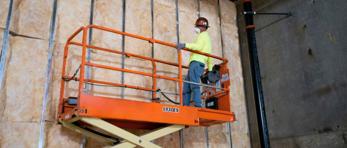 A worker installing pink fiberglass batt insulation on a lift.