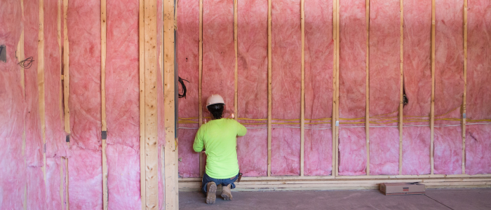 A person in a yellow shirt installs pink fiberglass batt insulation.