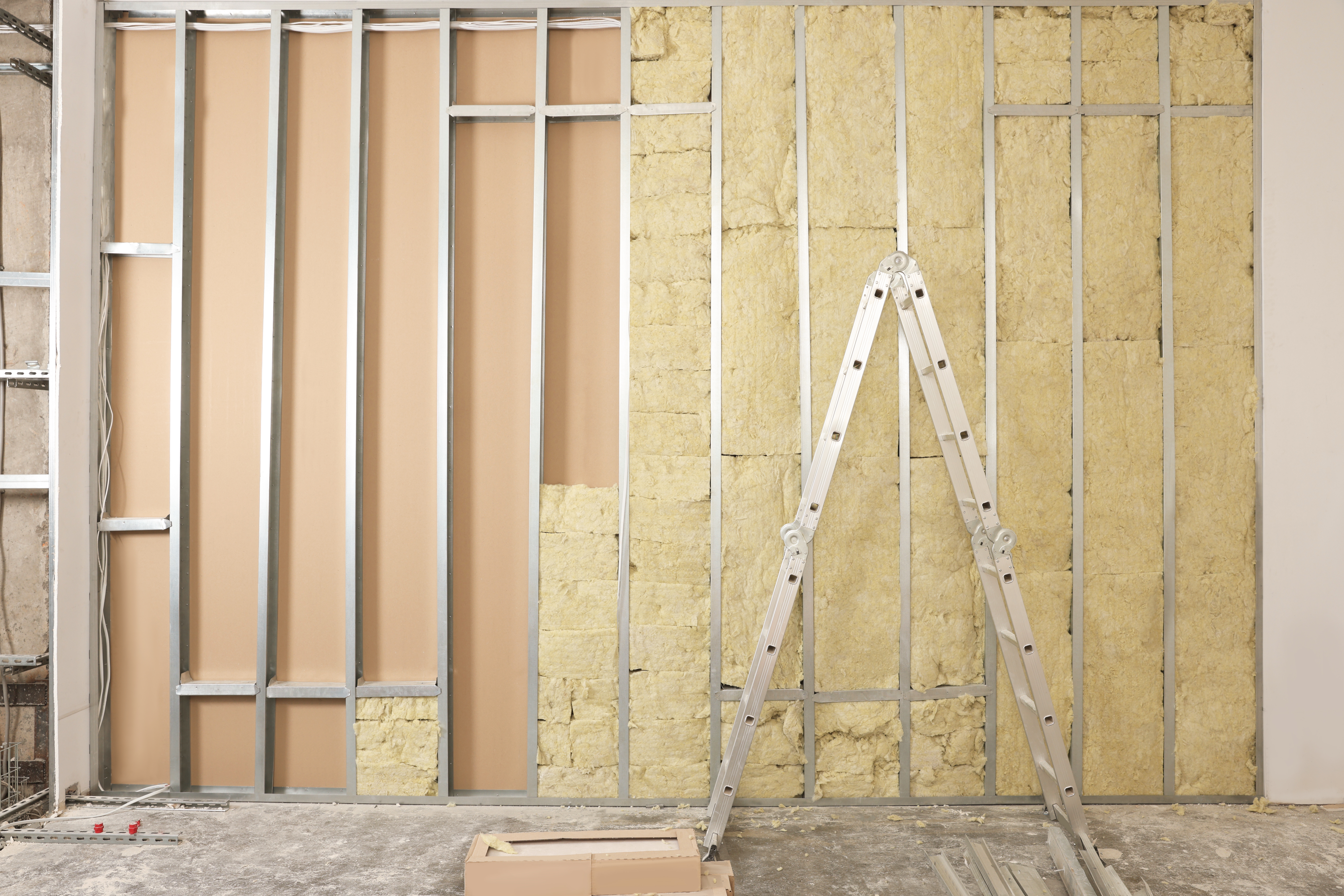 Metal studs with fiberglass batt insulation with a metal ladder in the foreground.